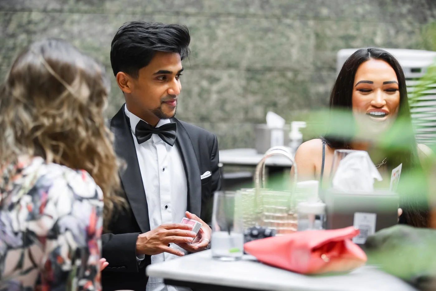 Nabeel holds a deck of cards while talking with guests at a table.
