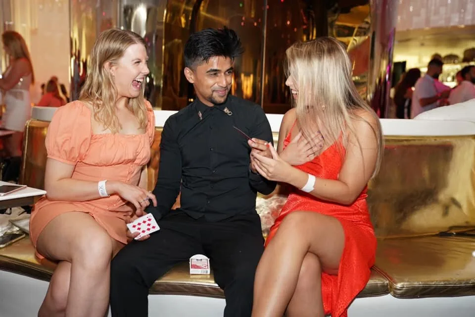 Nabeel performs card magic for two seated guests.