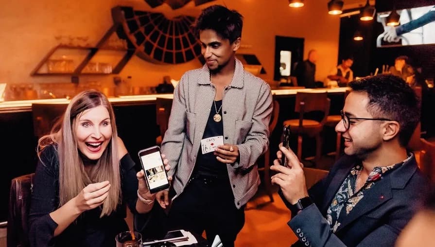 Guests react to Nabeel performing a card trick at a table.