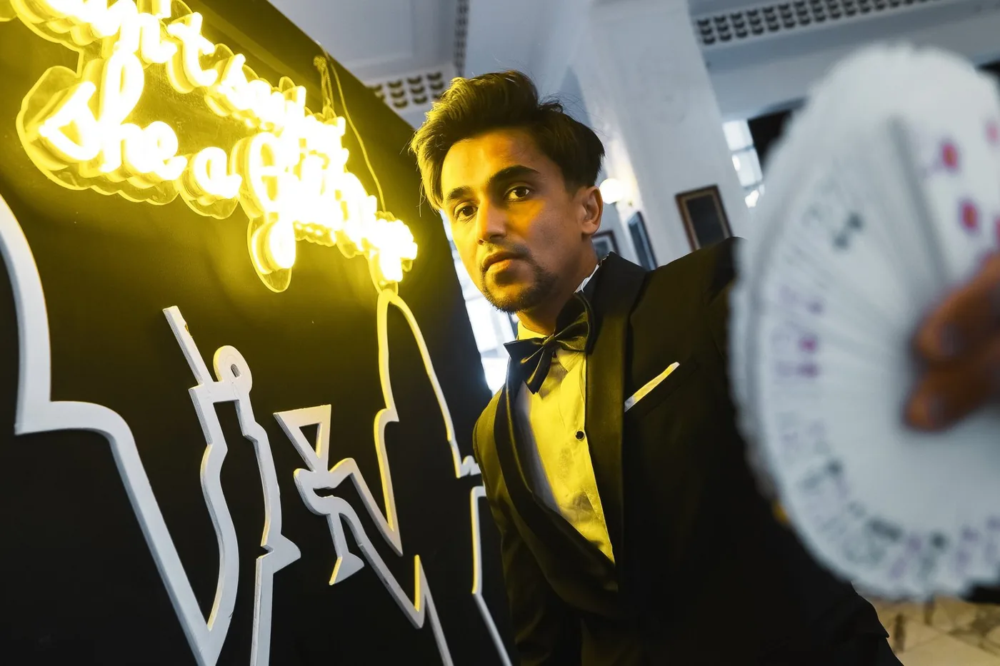 Nabeel holds a playing card towards the camera beside gold-lit lettering.